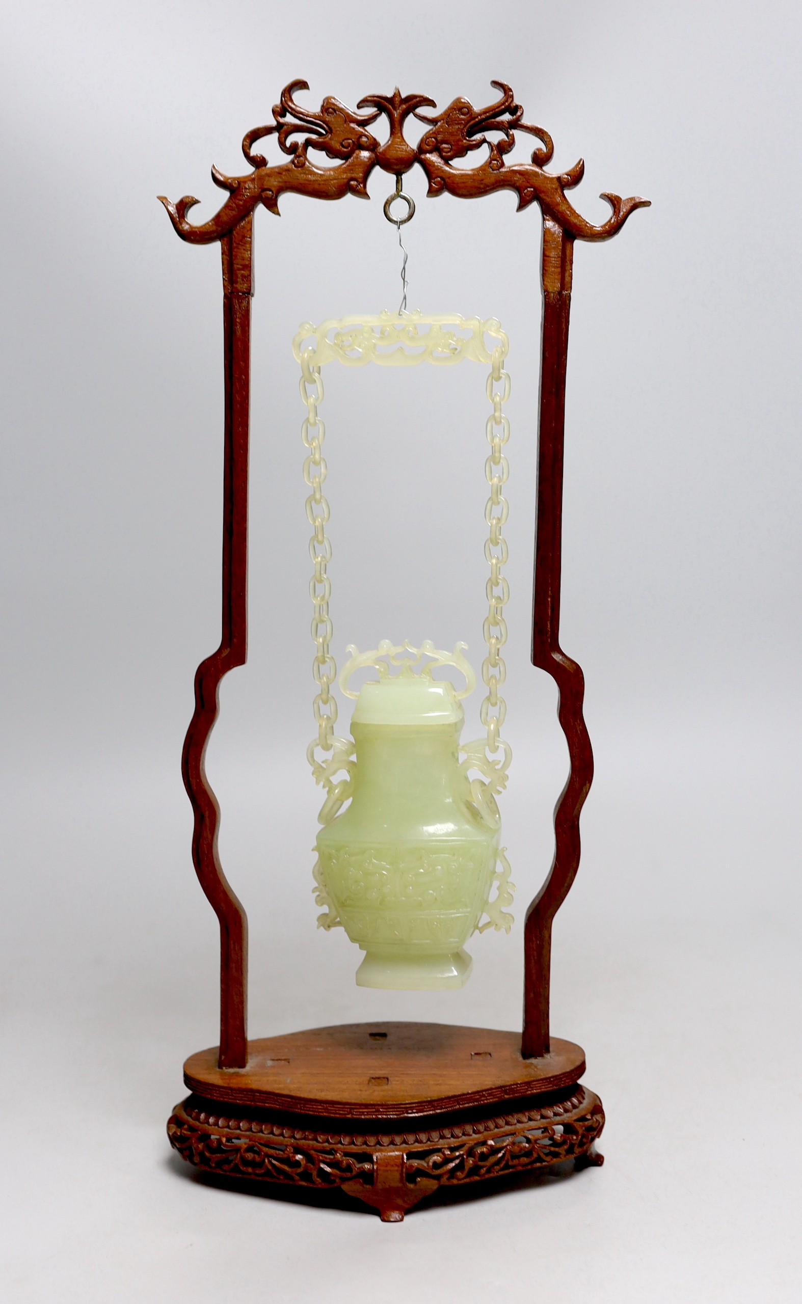 A Chinese bowenite jade hanging vase and cover together with a carved hard wood stand, one foot missing, 42cm tall